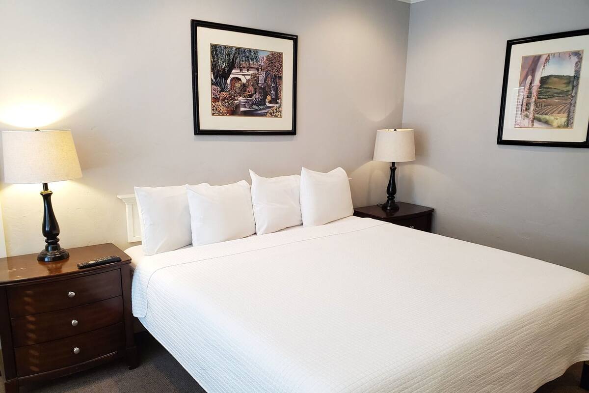Une chambre d’hôtel avec un grand lit, deux tables de chevet avec des lampes, une commode et deux tableaux encadrés accrochés aux murs.
