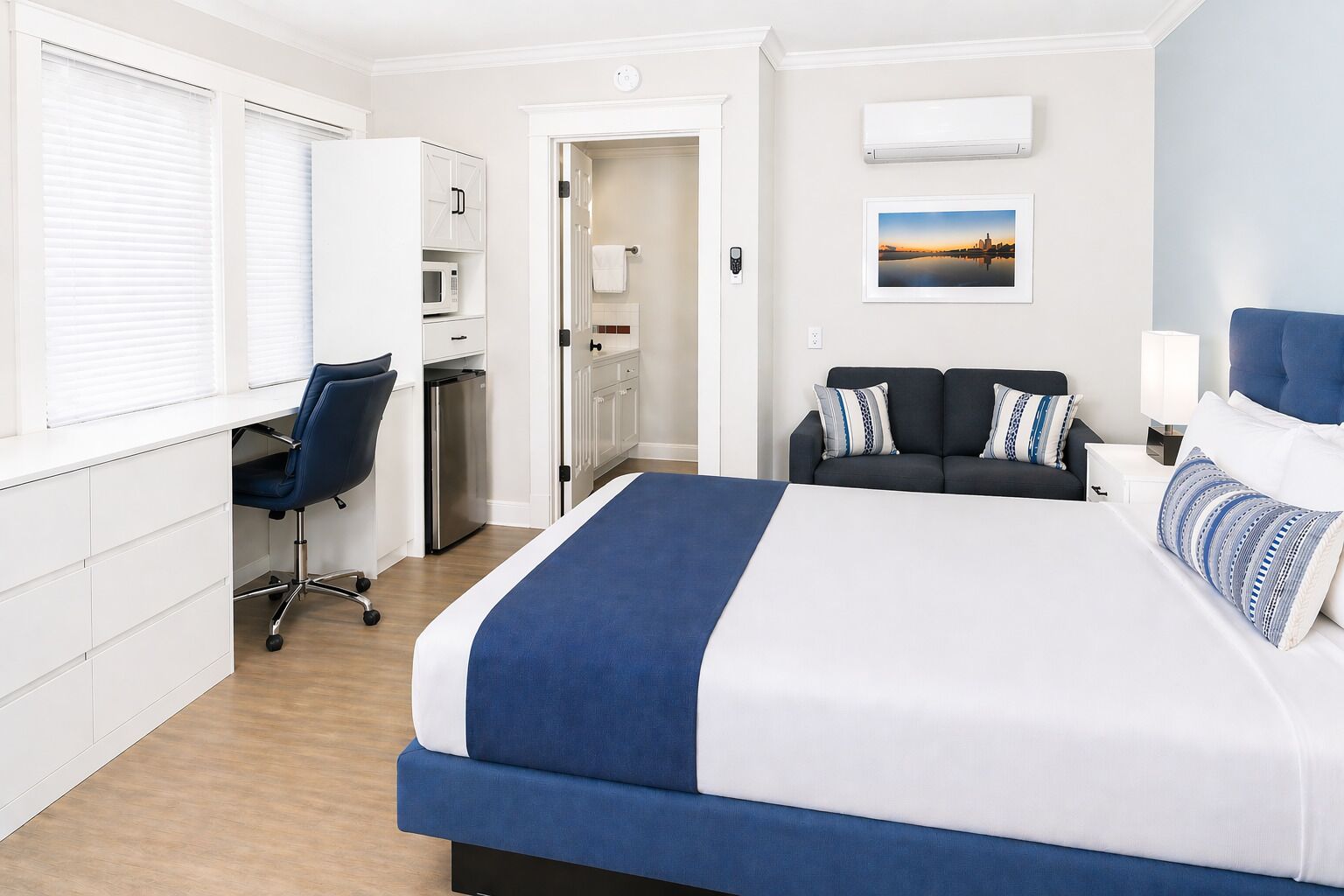 A hotel room with a bed, a desk, a chair, a microwave, a refrigerator, a TV, and a picture on the wall.