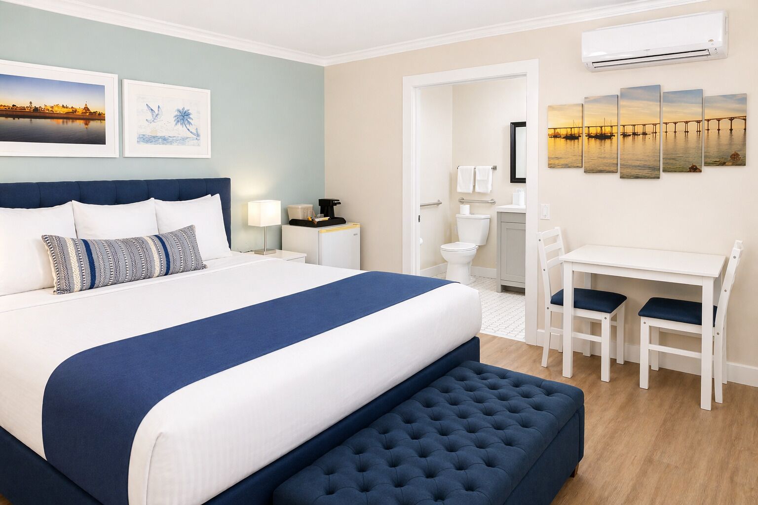 Habitación de hotel con una cama grande, un escritorio con dos sillas, un baño y obras de arte en las paredes.