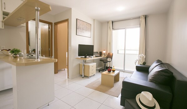 A modern living room with a black sofa, a small coffee table, a TV, and a kitchen area with a counter and cabinets. - Premier Residence Hplus Long Stay (Brasília)