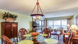 A dining area with a glass table, wicker chairs, a buffet bowl, and a television in the background. - A116-amelia-surf-and-racquet (Fernandina Beach)