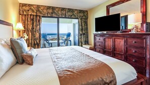 A hotel room with a large bed, a television, a wooden dresser, and a balcony with chairs. - A116-amelia-surf-and-racquet (Fernandina Beach)