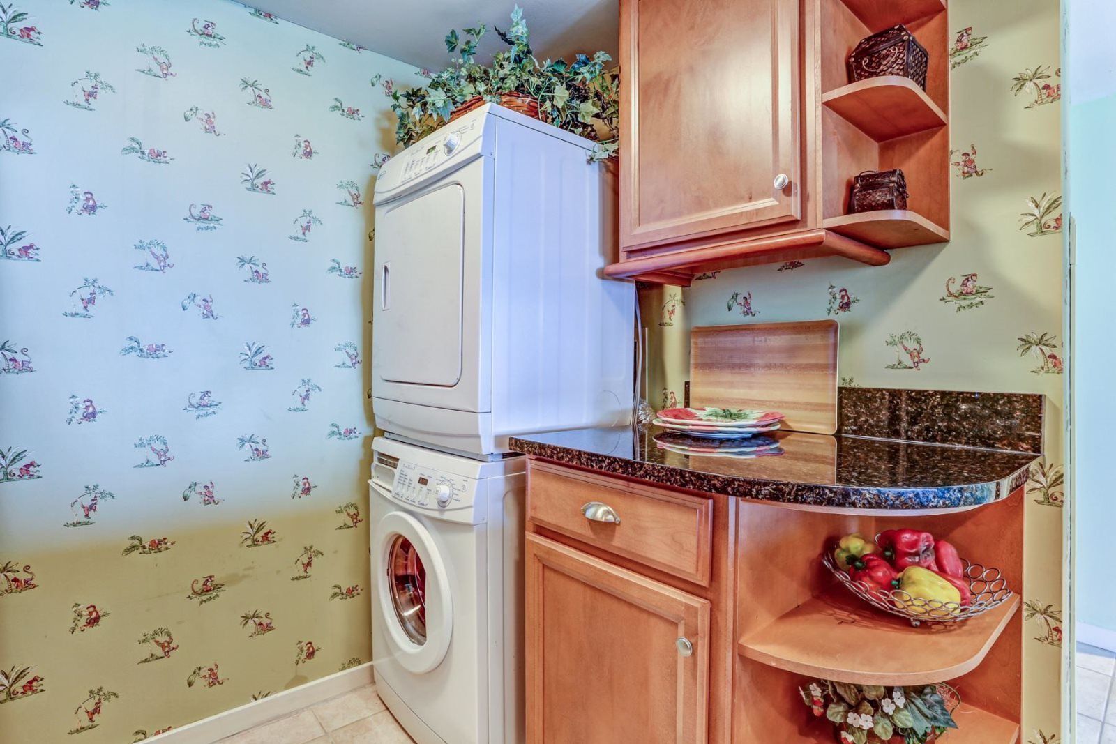 A compact kitchen with a washing machine, wooden cabinets, and a fruit bowl.