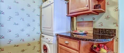 A compact kitchen with a washing machine, wooden cabinets, and a fruit bowl.