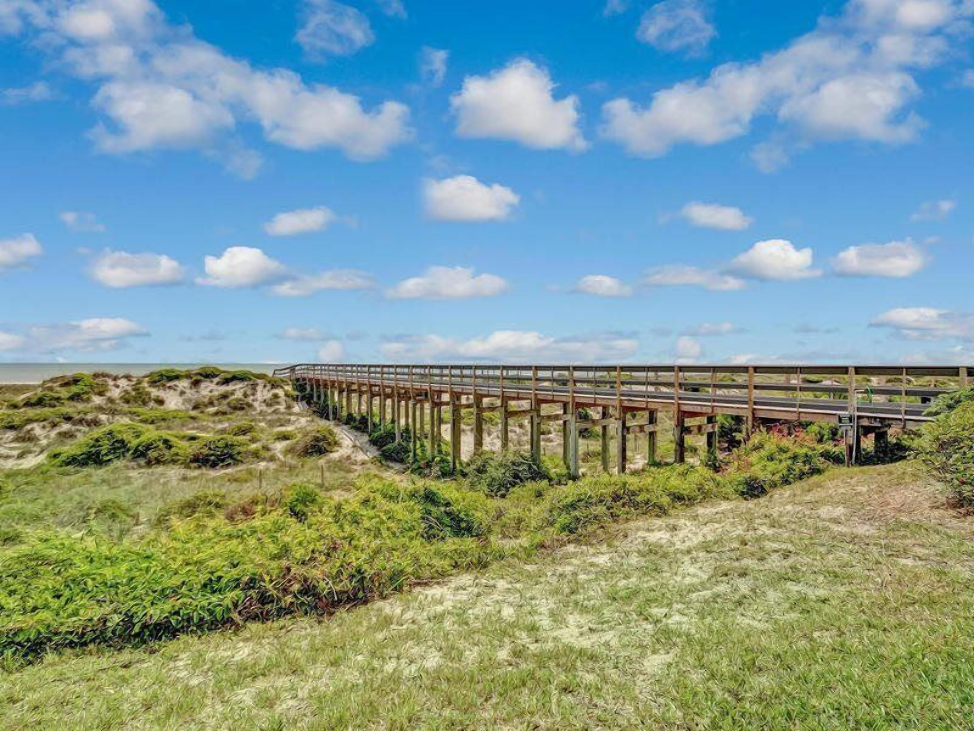 A coastal bridge with a clear sky and dunes in the foreground.