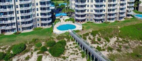 Un hôtel de grande hauteur doté de nombreux balcons, d’une piscine et d’un pont d’accès à la plage.