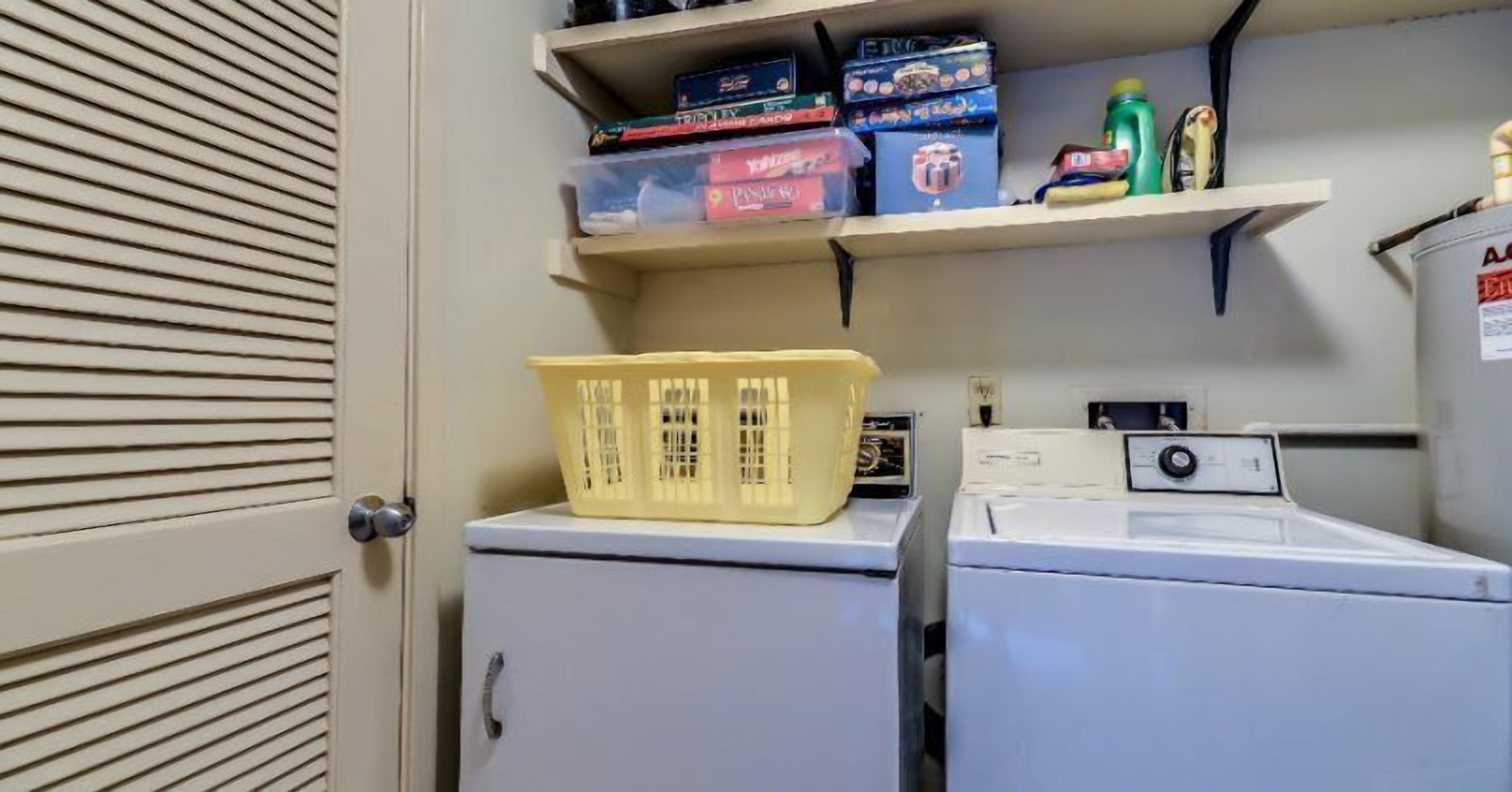 A laundry room with a washing machine, a dryer, and shelves above containing cleaning supplies and storage bins.