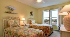 A room with two beds, a ceiling fan, a window with curtains, and a lamp.