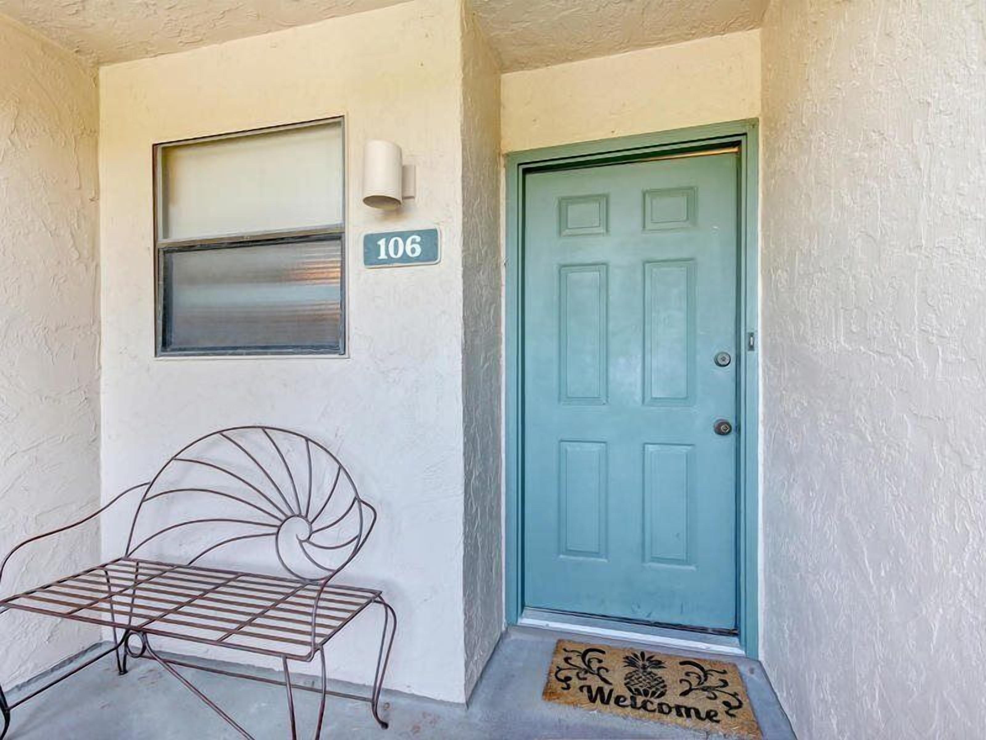 A door with a number 106 sign, a metal bench, and a welcome mat.