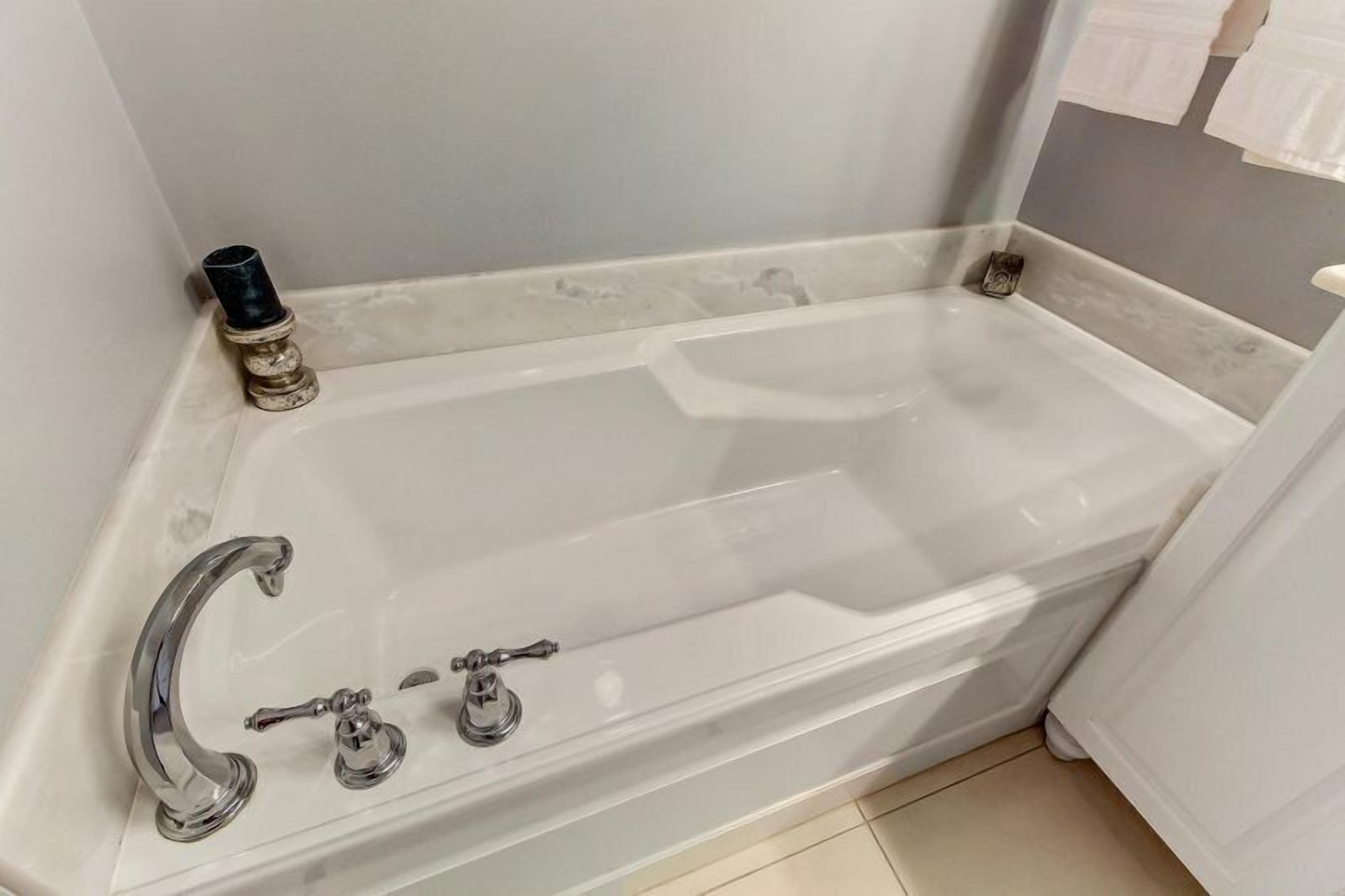 A bathroom with a white bathtub, two faucets, and a small black object on the left side.
