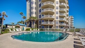 A swimming pool with lounge chairs, a building with multiple balconies, and palm trees. - 2-ocean-place (Fernandina Beach)