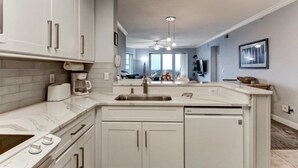 A modern kitchen with white cabinets, a built-in dishwasher, and a large island with a sink. - 2-ocean-place (Fernandina Beach)