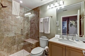 Une salle de bain avec un mur de douche en marbre, des toilettes, un lavabo avec un miroir et un porte-serviettes.