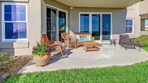 A covered patio with outdoor furniture, including chairs and a sofa, near a building with large windows and sliding glass doors. - 2-ocean-place (Fernandina Beach)