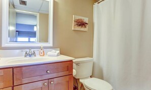A bathroom with a white sink, mirror, and toilet. There is a towel on the counter and a picture on the wall. - 106-atlantis-on-amelia (Fernandina Beach)