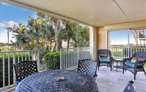A covered outdoor seating area with a round table and chairs, surrounded by a white railing. - 106-atlantis-on-amelia (Fernandina Beach)