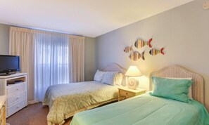 A bedroom with two beds, a TV, and a wall with fish decorations. - 106-atlantis-on-amelia (Fernandina Beach)