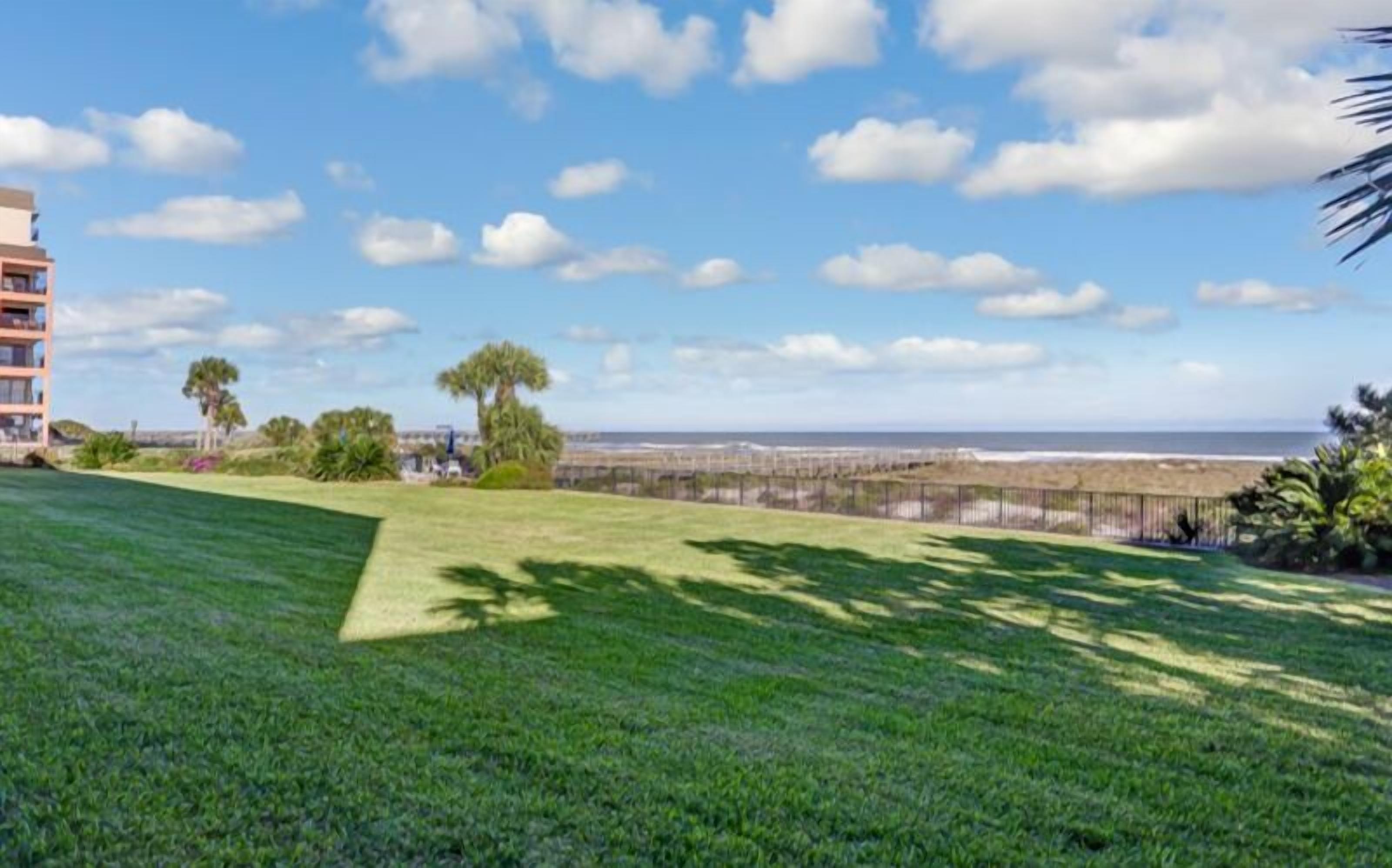 A grassy area with a view of the ocean and a building in the background.