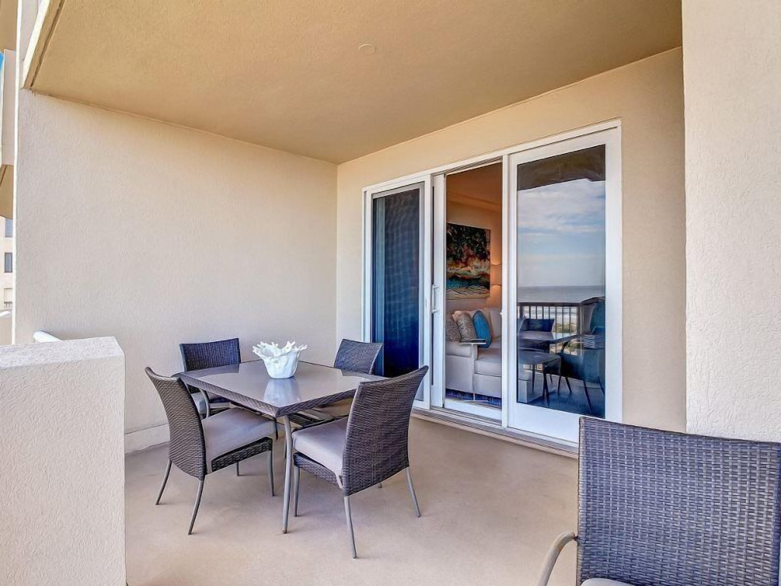A balcony with a table and chairs, a sliding glass door leading to a seating area with a view.