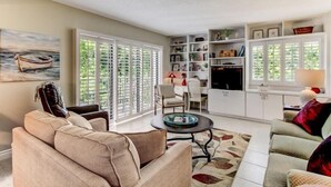 A living room with a sofa, armchair, coffee table, and a bookshelf. - 2126 Beachwood (Fernandina Beach)