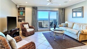 Un salon équipé d’un téléviseur, de meubles en osier, d’un canapé et d’un balcon avec vue.