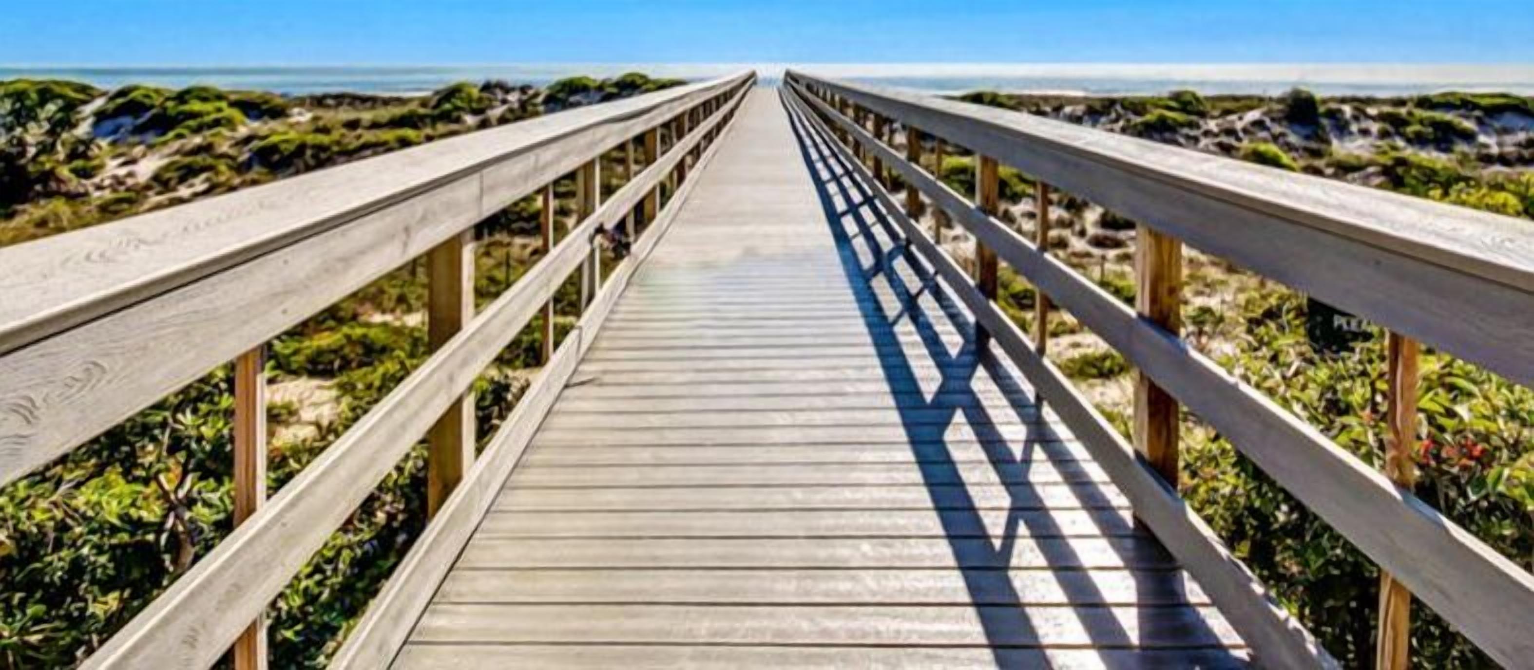 A wooden boardwalk leading to a beach with a clear view of the ocean.