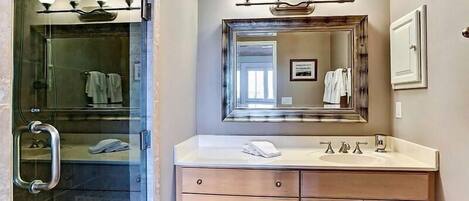 A bathroom with a glass shower enclosure, a vanity with a mirror and lights, and wooden cabinets.