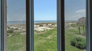 Vista a través de una ventana con una playa y una estructura de madera al fondo.