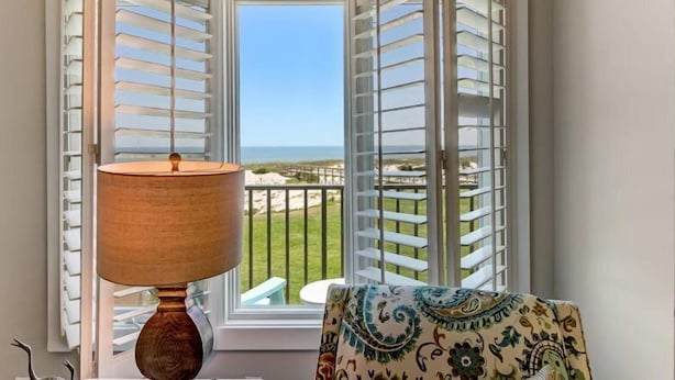 Una habitación con vista a la playa, una mesa con lámpara y una silla estampada.