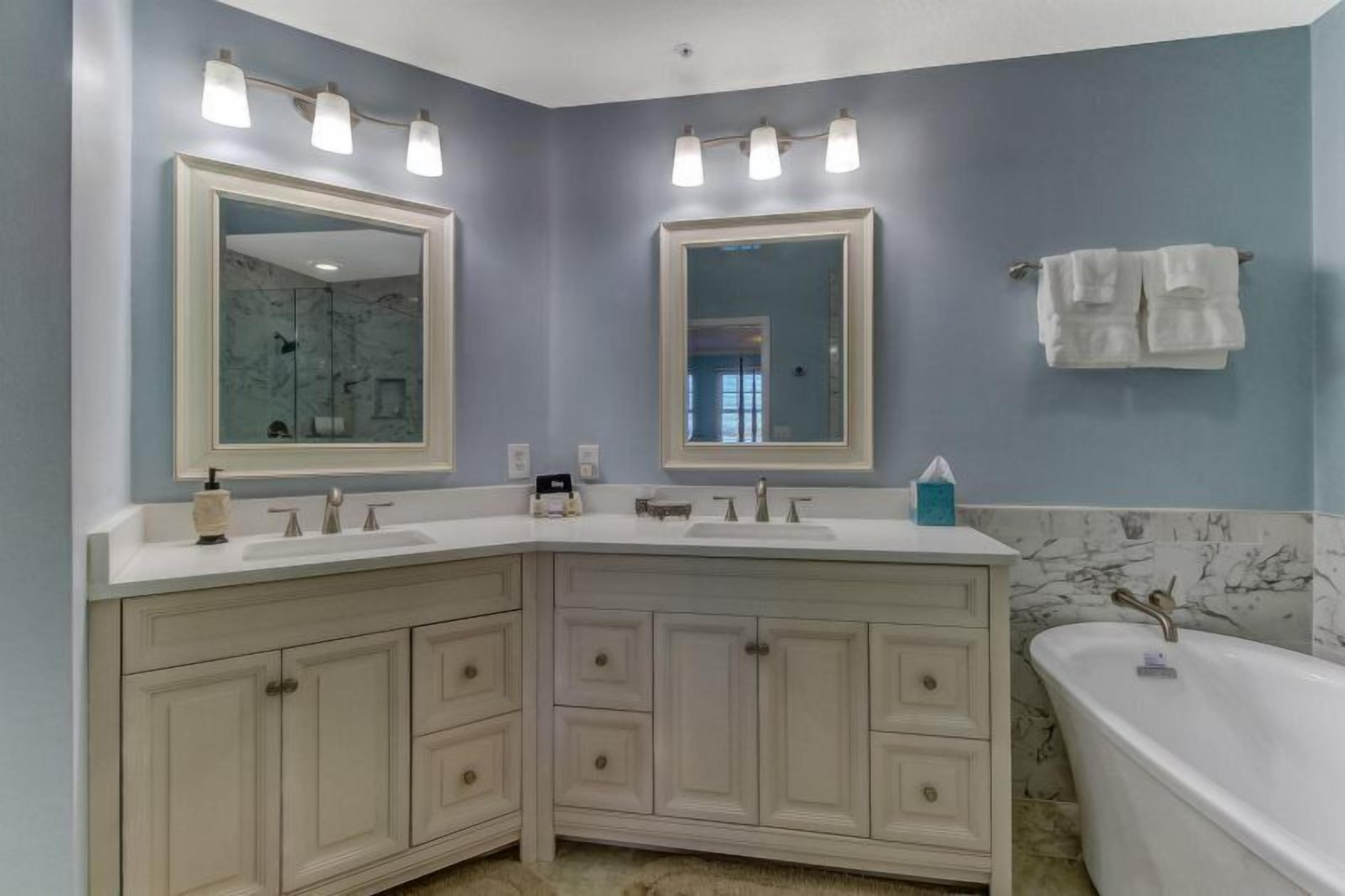 A bathroom with a double vanity, two large mirrors, a bathtub, and a towel rack.
