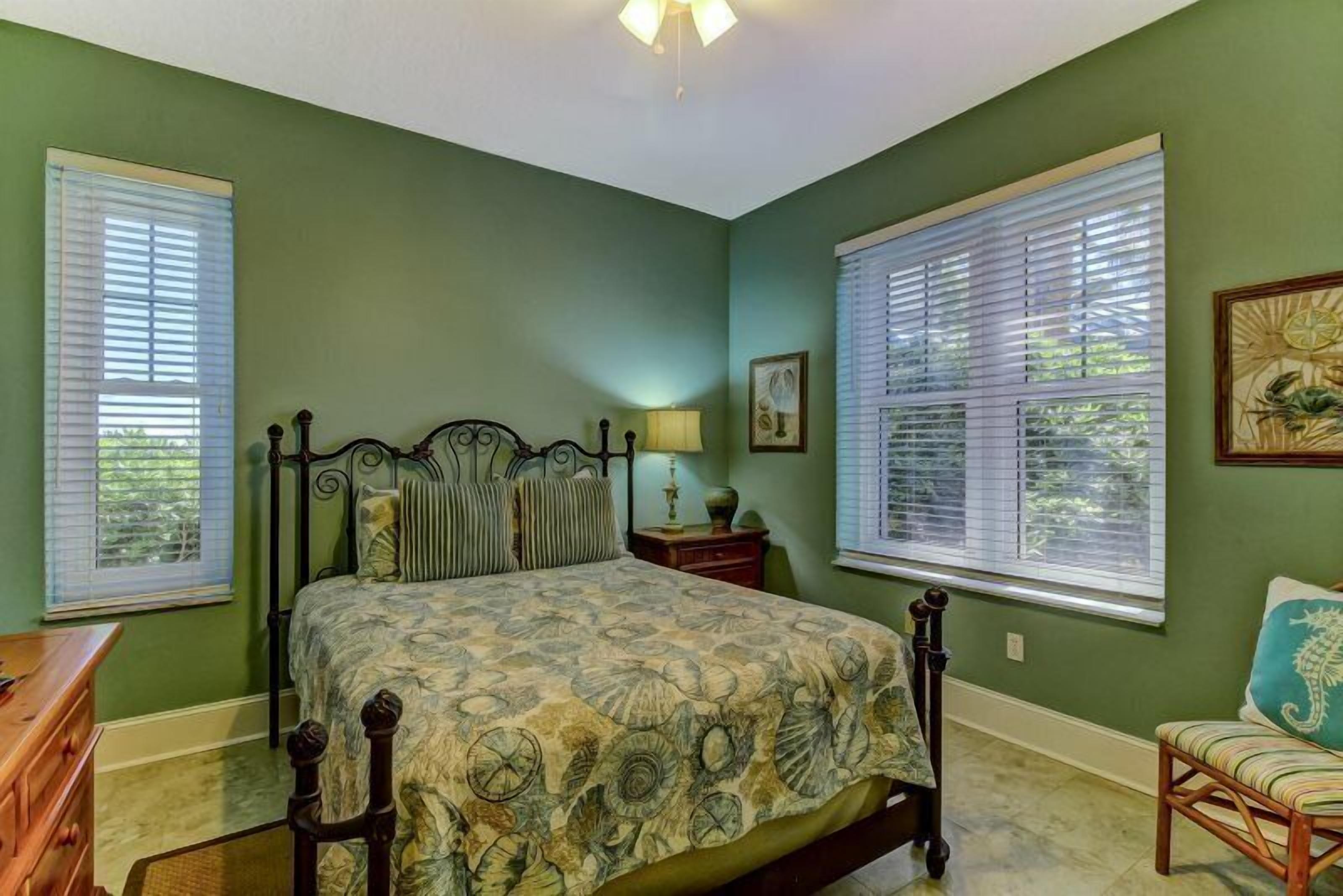 A bedroom with a bed, a nightstand, a chair, and two windows with blinds.