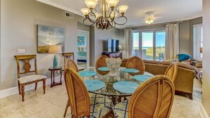 A dining area with a glass table surrounded by wicker chairs, a chandelier, and artwork on the walls. - 5-ocean-place (Fernandina Beach)
