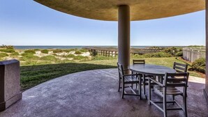 An outdoor patio with a table and chairs, overlooking a beach and dunes. - 5-ocean-place (Fernandina Beach)