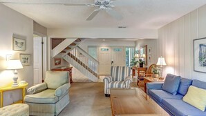 A spacious living room with a high ceiling fan, a staircase, and a blue sofa. - 2135-beachwood (Fernandina Beach)