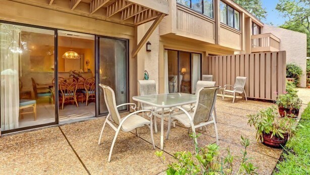 A modern outdoor patio with a glass door leading to a dining area, a table with chairs, and potted plants. - 2135-beachwood (Fernandina Beach)