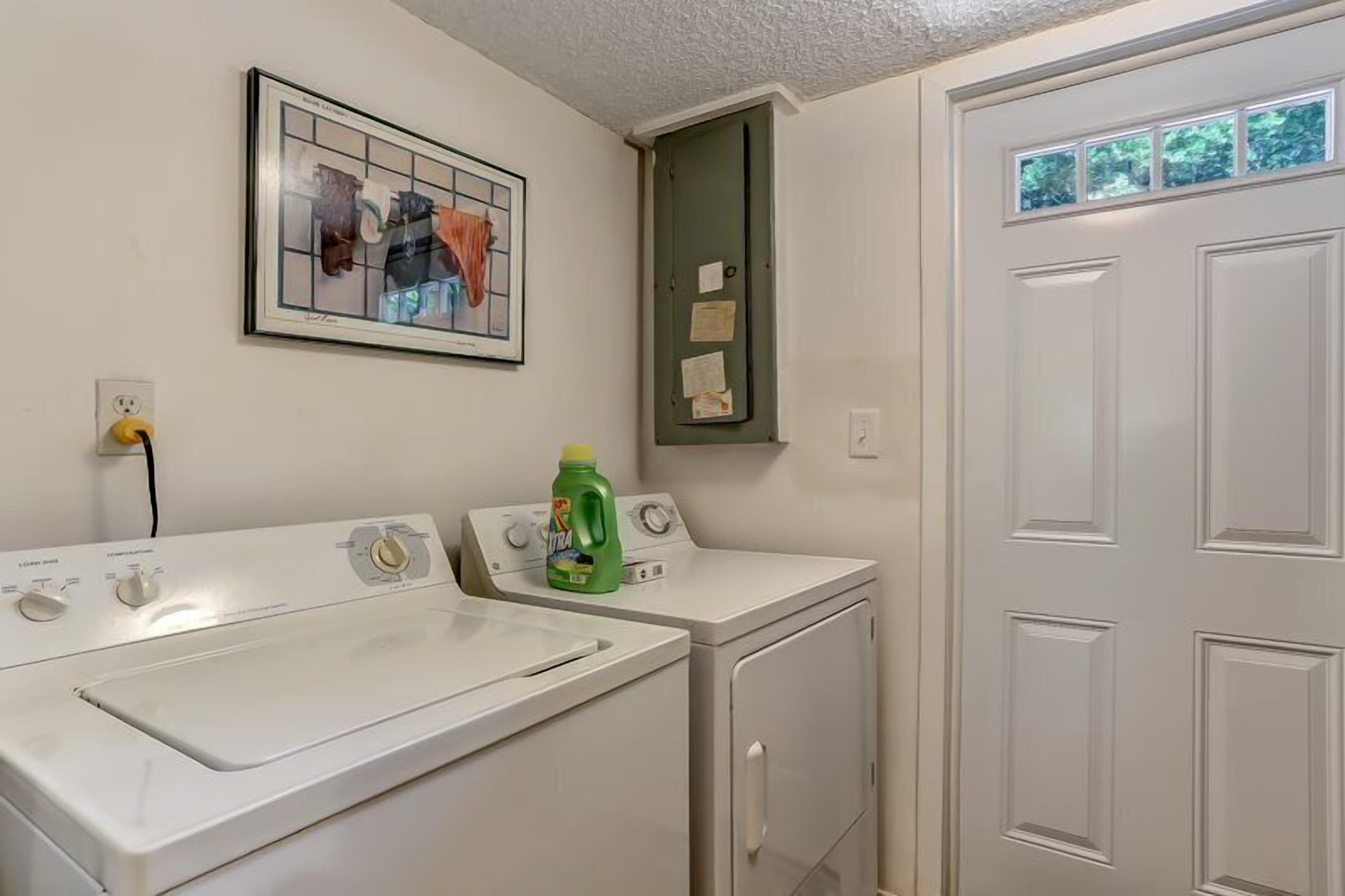 Un cuarto de lavandería con dos lavadoras y una secadora, un mueble de baño verde y una obra de arte enmarcada en la pared.