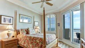 A four-poster bed with a floral bedspread, a ceiling fan, and a view of the ocean through a sliding glass door. - 69-ocean Place (Fernandina Beach)