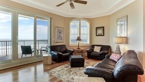 A spacious living room with a large sliding glass door leading to a balcony, a ceiling fan, and a view of the ocean. - 69-ocean Place (Fernandina Beach)