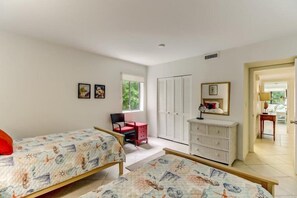 Een slaapkamer met twee bedden, een dressoir, een stoel en een raam met luiken.