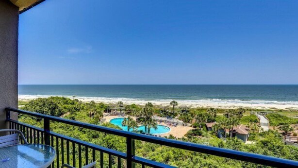A balcony with a view of a beach, a pool, and a resort area.