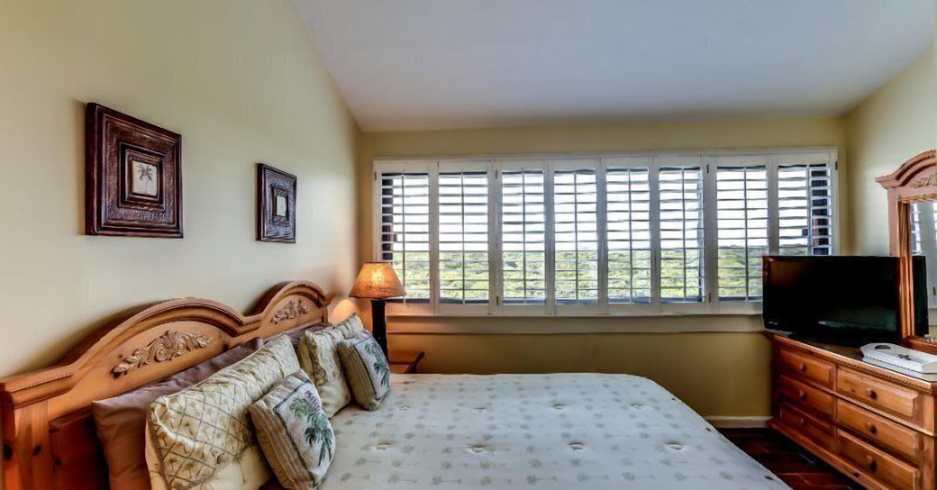 A bedroom with a bed, a dresser, a television, and a window with blinds.