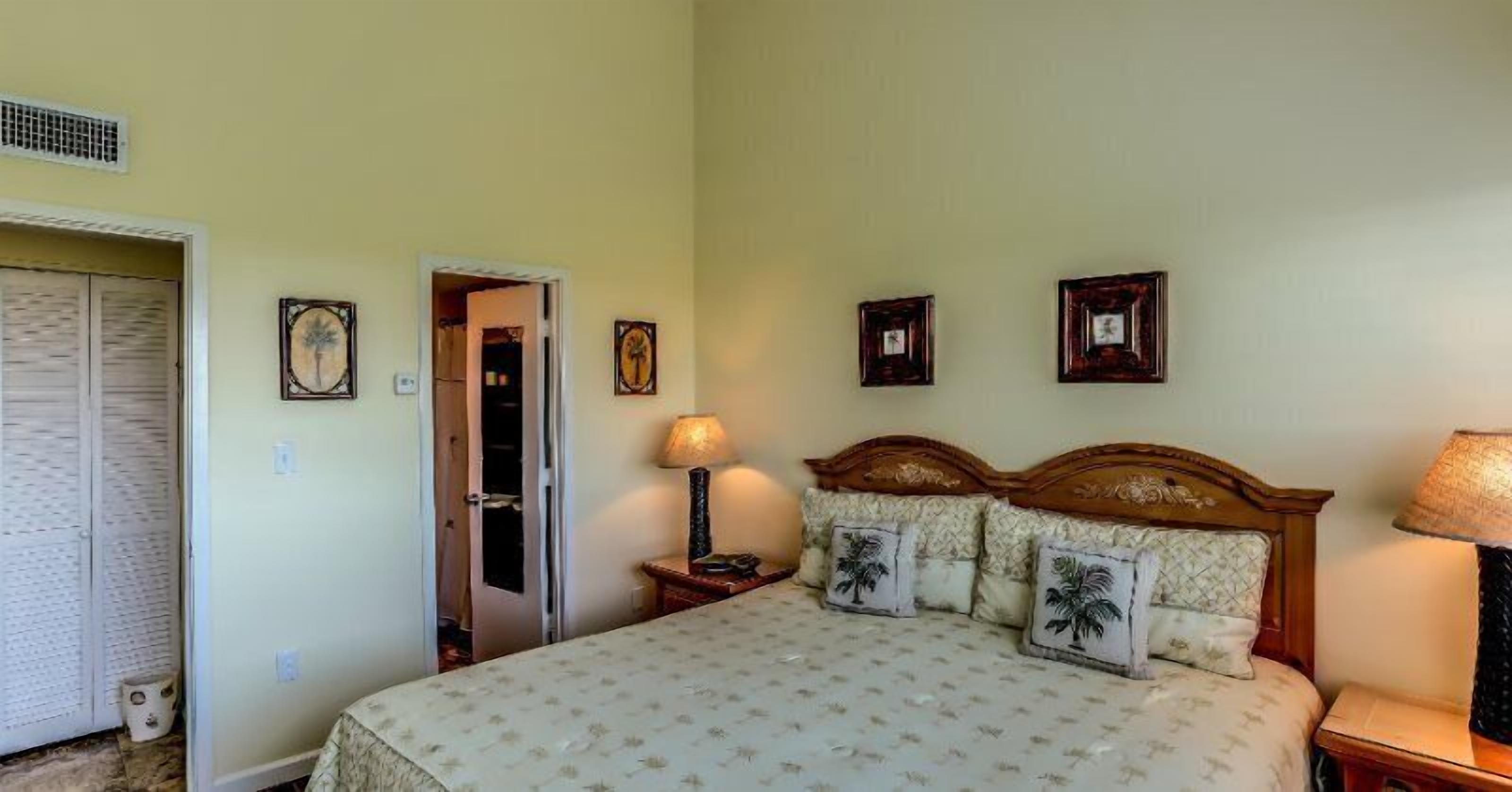 A bedroom with a bed, bedside lamps, a door, and framed pictures on the wall.