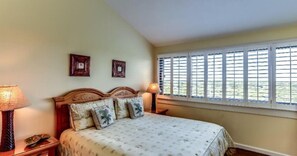 A bedroom with a bed, two bedside lamps, a window with shutters, and two framed pictures on the wall. - 1140-beach-walker (Fernandina Beach)