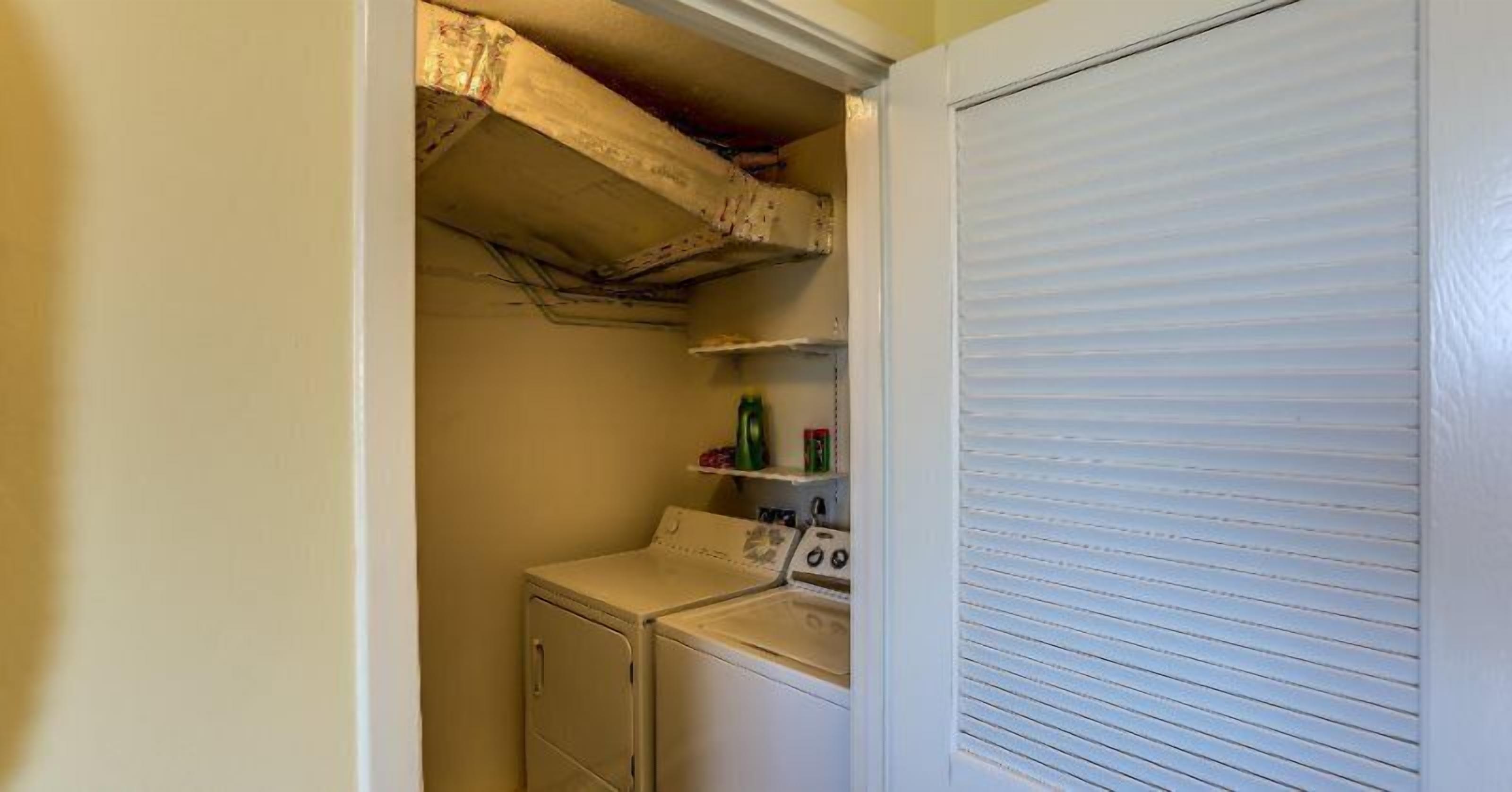 A laundry room with a washing machine, dryer, and shelves with laundry supplies.