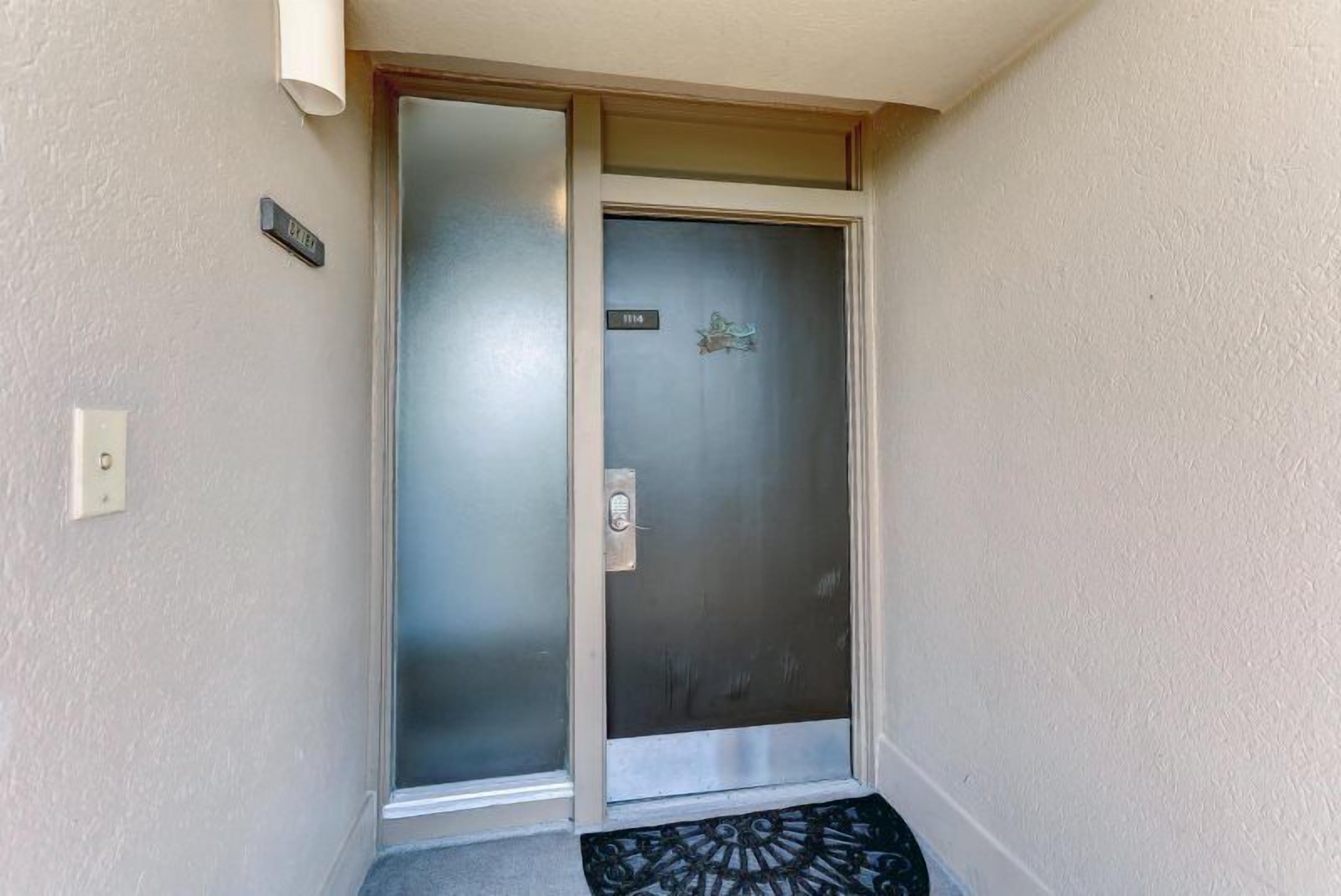 En dörr med en panel av frostat glas och ett handtag av metall, en liten skylt ovanför och en svart dörrmatta vid ingången.