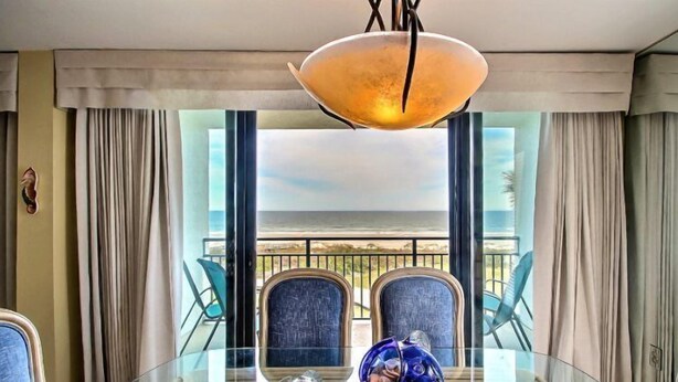 A dining area with a glass table, blue chairs, and a view of the outdoors. - 1182-beach-walker (Fernandina Beach)