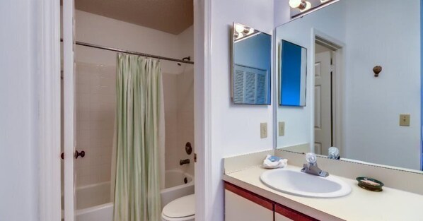 A bathroom with a shower, toilet, sink, and a large mirror.