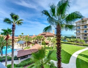 A resort with a pool, palm trees, and a view of the ocean. - 1428-windsong (Fernandina Beach)