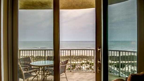 A balcony with a table and chairs, overlooking a beach with a railing. - 59-ocean-place (Fernandina Beach)