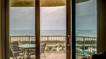 Varanda com mesa e cadeiras, vista para uma praia com guarda-corpo.